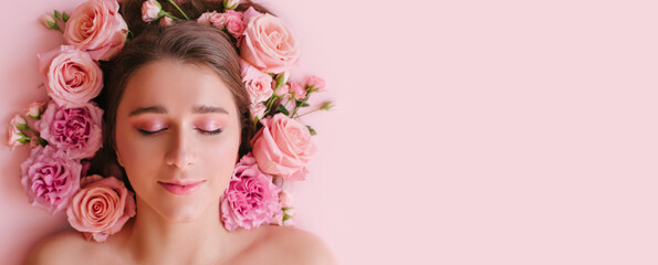 Close up portrait of beautiful woman face wih bright make up and perfect skin posing with roses on pink background.