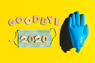 Words GOODBYE 2020 from wooden letters, inflated medical glove waving bye-bye and facemask on a...