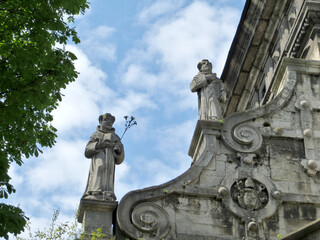 Fototapeta na wymiar Stone figures of monks against the blue sky with clouds on the ridge of the cathedral building. Bernardine Church