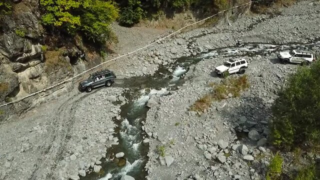 Off Road vehicles crossing wild mountain river. Aerial view of suv cars