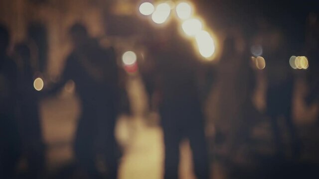 Defocused silhouettes of dancing couples in the night street in slow motion tracking shot.