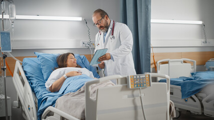 Obraz premium Hospital Ward: Friendly Latin Doctor Talks to Beautiful Female Patient Resting in Bed, Shows Tablet Computer, Explains Test Results. Physician Talks to Woman Recovering after Successful Surgery