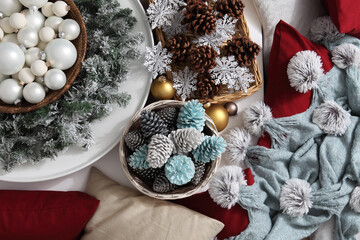 top view christmas decorations centerpiece with garland and balls near a basket with colorful pine cones, isolated on a white table amidst the sofa cushions