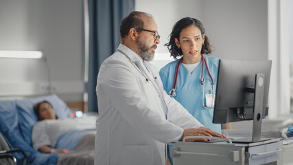 Fototapeta premium Hospital Ward: Latin Doctor Talks With Professional Head Nurse, They Use High-Tech Touchscreen Computer. In Background Patient in Bed Recovering after Successful Surgery. Health Care Specialists