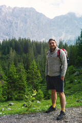 A young man in the mountains who is very happy about hiking and mountain sports. He is bearded and looks very much like a nature boy. In the background you can see the Alps and the Zugspitze