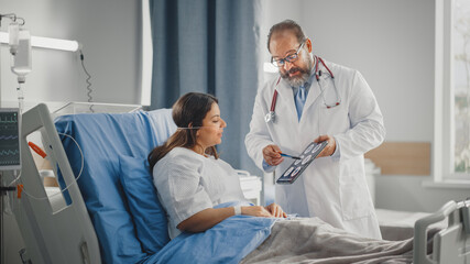 Hospital Ward: Friendly Latin Doctor Talks to Beautiful Smiling Female Patient Resting in Bed, Uses Tablet Computer, Explains Her Brain Scan Results. Physician Talks to Woman Recovering after Surgery