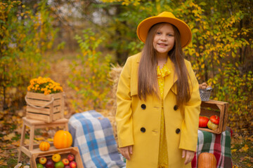 Obraz premium cute beautiful teenage brunette girl in an orange hat, dress and coat next to autumn decorations - pumpkins, apples, blankets, hay. Cosiness