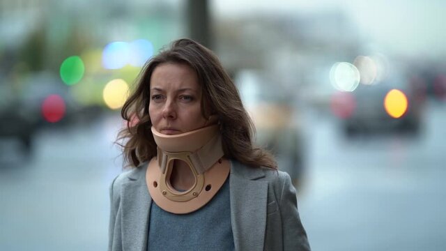 middle-aged woman with osteochondrosis and neck ache is walking on city street, wearing cervical collar for curing