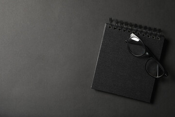 Glasses, notebook and space for text on dark background, top view. Black Friday concept