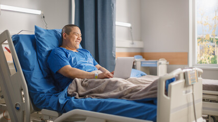 Medical Hospital Ward: Happy Smiling Chinese Man Resting in Bed and Using Laptop Computer to Video Chat with His Family, Friends, Watching Funny Videos. Businessman Recovering after Surgery.