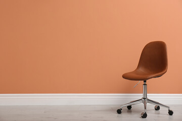 Modern office chair near orange coral wall indoors. Space for text