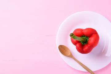 Red bell pepper on white plate with wooden spoon on pink background, Top view