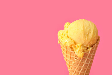 Delicious yellow ice cream in waffle cone on pink background, closeup. Space for text