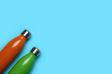 Modern thermo bottles on light blue background, flat lay. Space for text