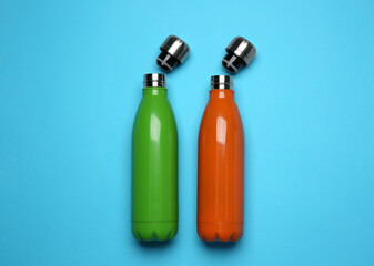 Modern thermo bottles on light blue background, flat lay