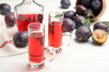 Delicious plum liquor and ripe fruits on white wooden table, closeup. Homemade strong alcoholic beverage