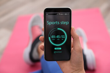 Young woman using fitness app on smartphone indoors, closeup