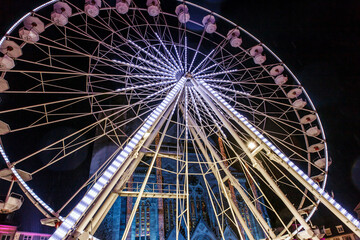 Fototapeta premium A ferris wheel sparkling with neon signs, and a cathedral decorated with Christmas decorations visible between it. Mulhouse, france