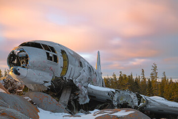 Miss Piggy Plane wreck in Churchill, Manitoba with blue sky and cloudy sunset background in frame with snow on rocks in front of crash landing site. 