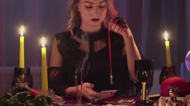 Female fortune teller holding a magic pendulum over a candle