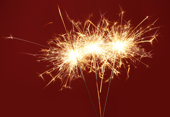 Bright burning sparklers on red background, closeup