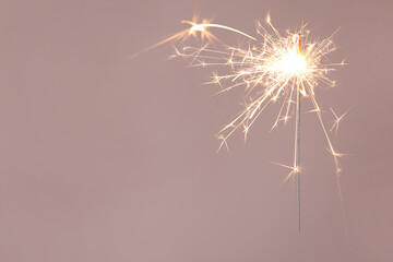 Bright burning sparkler on beige background, closeup. Space for text - Powered by Adobe