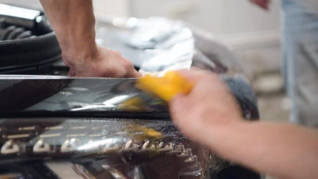 Close up of paint protection film installation on modern luxury car. PPF is polyurethane film that wrap car paint to protect paint surface from stone chips, bug splatter, and abrasion