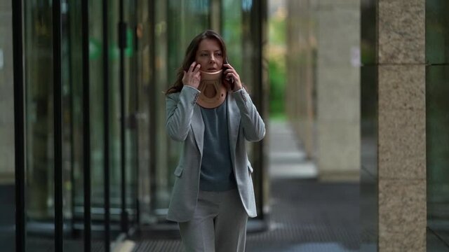 modern businesswoman is talking by phone at walking, wearing cervical collar for curing osteochondrosis
