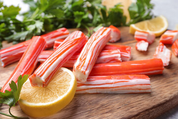 Delicious crab sticks with lemon and parsley on wooden board, closeup