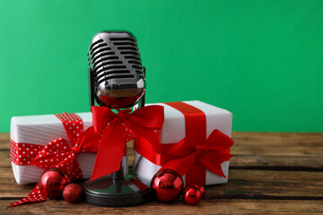 Retro microphone with red bow, gift boxes and festive decor on wooden table against green...