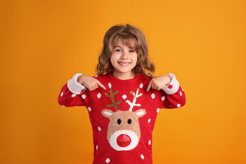 Cute little girl pointing at her red Christmas sweater against orange background