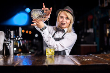 Focused girl bartending creates a cocktail while standing near the bar counter in pub