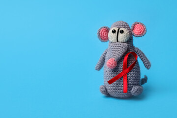 Cute knitted toy mouse with red ribbon on blue background, space for text. AIDS disease awareness
