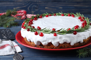 Traditional Christmas cake decorated with rosemary and cranberries on blue wooden table, closeup