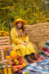 cute beautiful teenage brunette girl in an orange hat, dress and coat next to autumn decorations - pumpkins, apples, blankets, hay. Cosiness