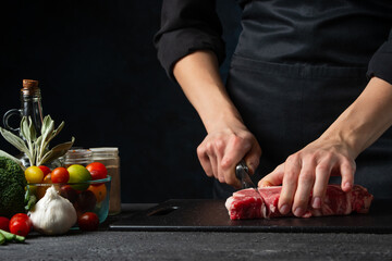 Close-up view of chef cuts with knife raw steak on wooden chopped board. Backstage of preparing...