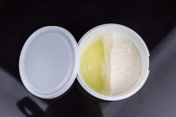Layer of whey protein formed on top of packaged yogurt after opening in dark background.