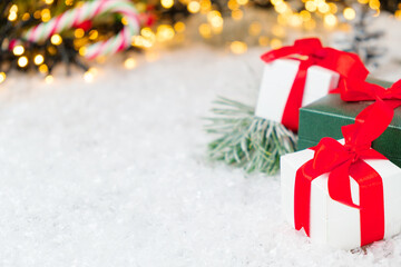 New year white and green gifts with red ribbon on the snow with copy space. Christmas composition