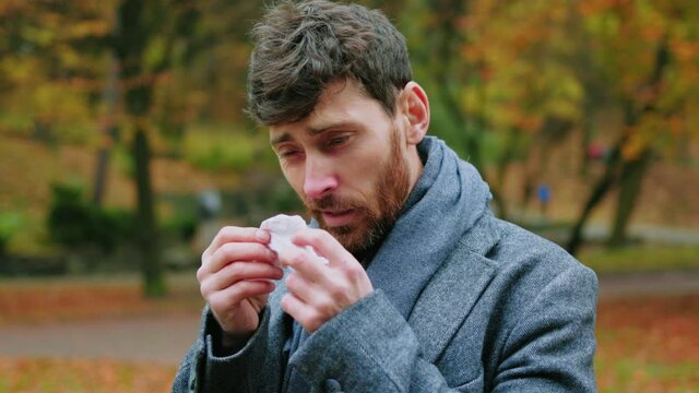 Portrait of sick handsome young man coughs has a runny nose uses a handkerchief. Virus face illness infection allergic. Sneeze. Close up. Slow motion