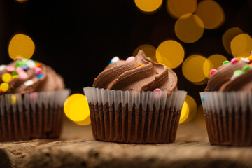 Close-up view of tasty chocolate cupcakes on rustic wooden table on black background with yellow lights. Sweet dessert. Bakery concept. Elegant food. Sweets for coffee or tea.