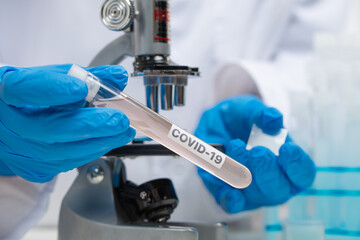Hands in protective blue gloves holds biological tube with covid-19 sample on microscope background. Research of coronavirus in laboratory. Healthcare and medical concept.
