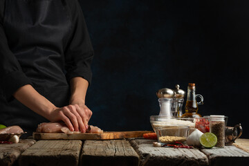 Fototapeta na wymiar Professional chef cuts with knife chicken fillet on chopped board. Backstage of cooking traditional Indian chicken curry on dark blue background. Frozen motion. Concept of cooking tasty hot meal.