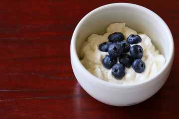 A close up shot of natural Greek style yogurt with some fresh blueberries on top in a white ceramic bowl.