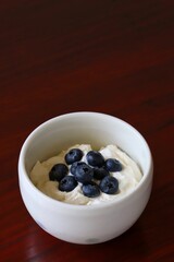 A close up shot of natural Greek style yogurt with some fresh blueberries on top in a white ceramic bowl.