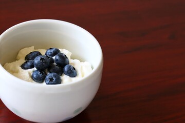 A close up shot of natural Greek style yogurt with some fresh blueberries on top in a white ceramic bowl.