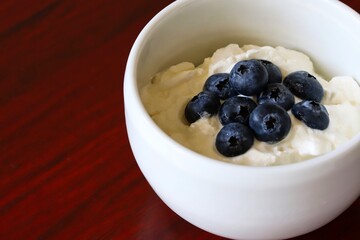 A close up shot of natural Greek style yogurt with some fresh blueberries on top in a white ceramic bowl.