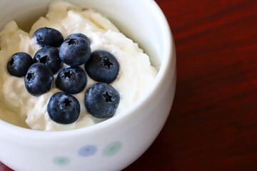 A close up shot of natural Greek style yogurt with some fresh blueberries on top in a white ceramic bowl.