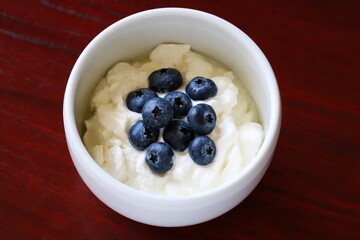 A close up shot of natural Greek style yogurt with some fresh blueberries on top in a white ceramic bowl.