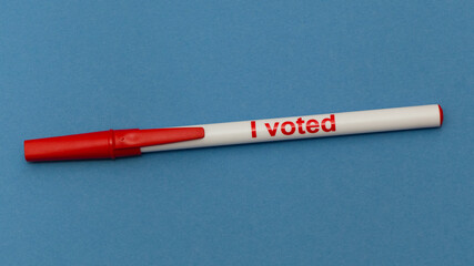 Close up horizontal color photo of red and white I voted ink pen on blue background with copy space.