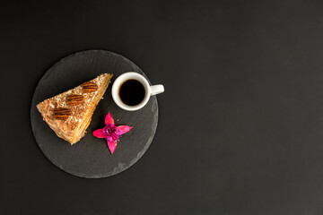 Obraz na płótnie Canvas A typical Portuguese cake made of cookies called Bolo de Bolasa with cream, pecans, black and white chocolate on a black slate with espresso and a flower on a black background. Flatlay. Copy space